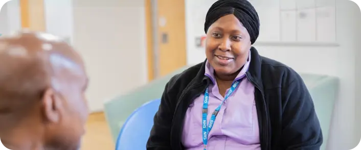 a female clinical worker in an NHS lanyard speaks with a man in a clinical setting