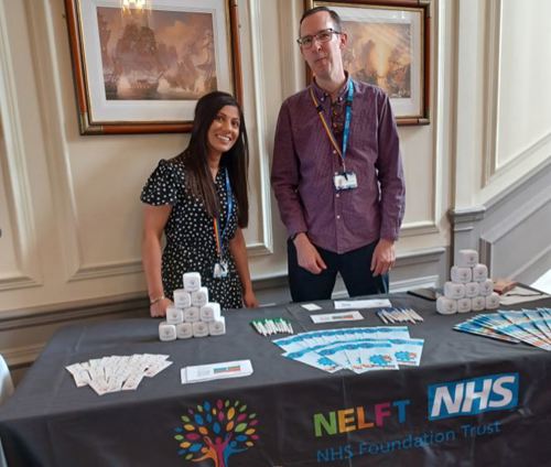 two smiling staff members behind a trust stand at a conference