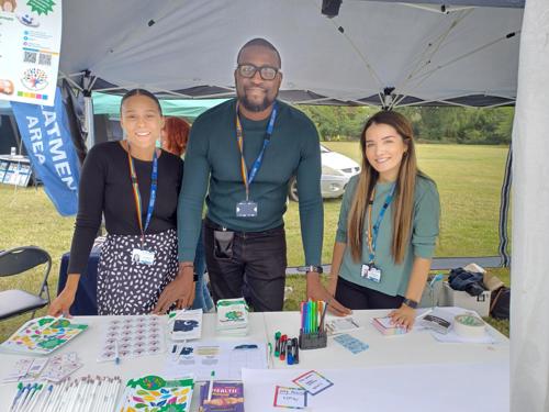 Three smiling staff members at a trust stall outside.