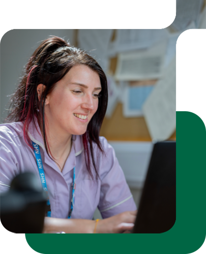 a female nhs nurse smiles as she works at a laptop