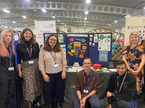 six smiling staff members at a wellbeing trust stall at a convention